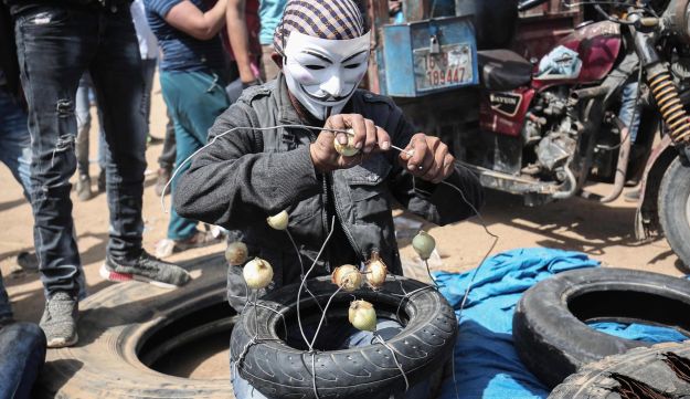 A Palestinian man wearing an Anonymous mask prepares to protest with onions to the effects of tear gas at the Israel-Gaza border, April 6, 2018.